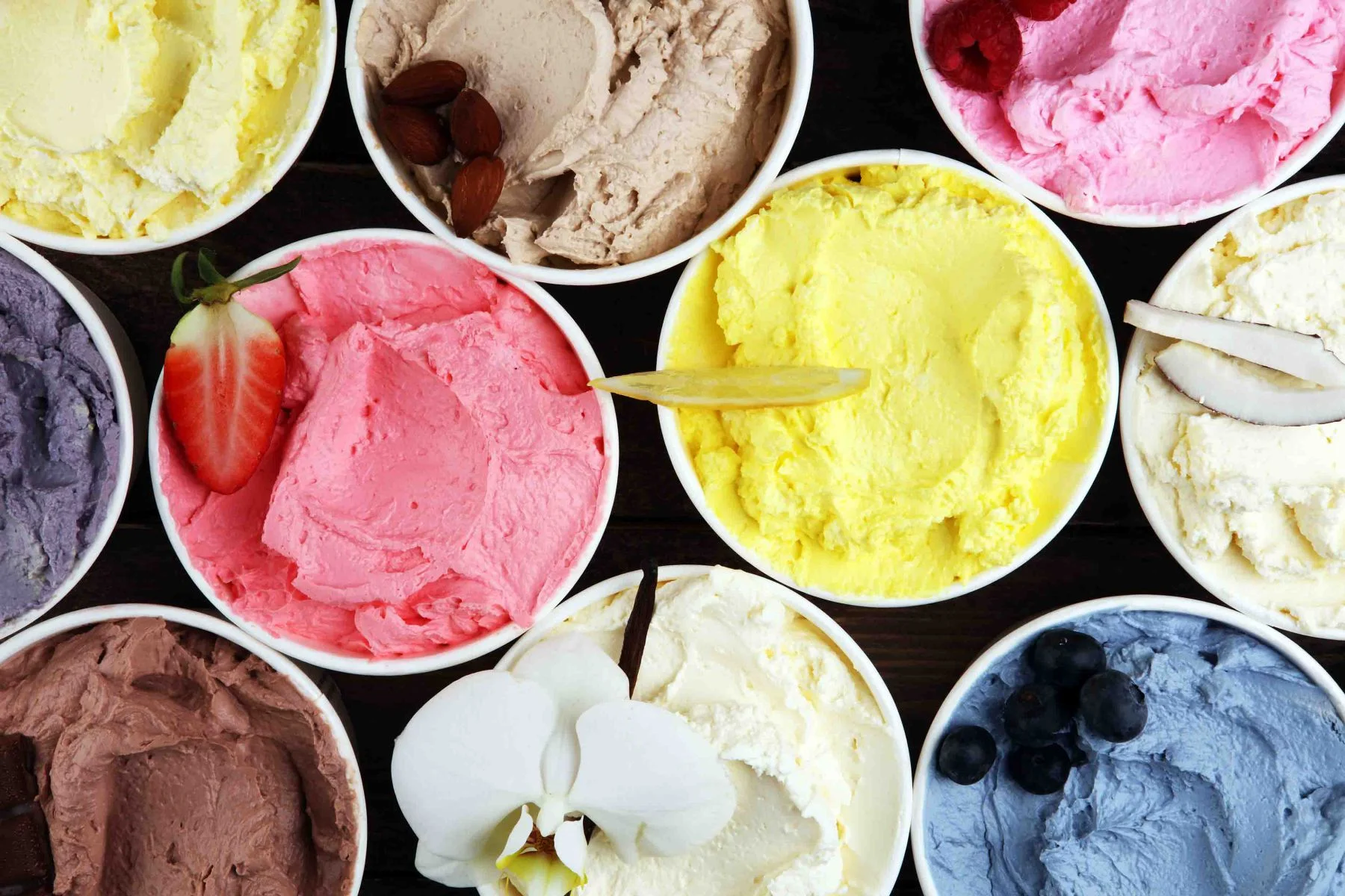 Verschiedene Eissorten mit frischen Blaubeeren, Erdbeeren, Kiwi, Zitrone und Vanille auf rustikalem Hintergrund